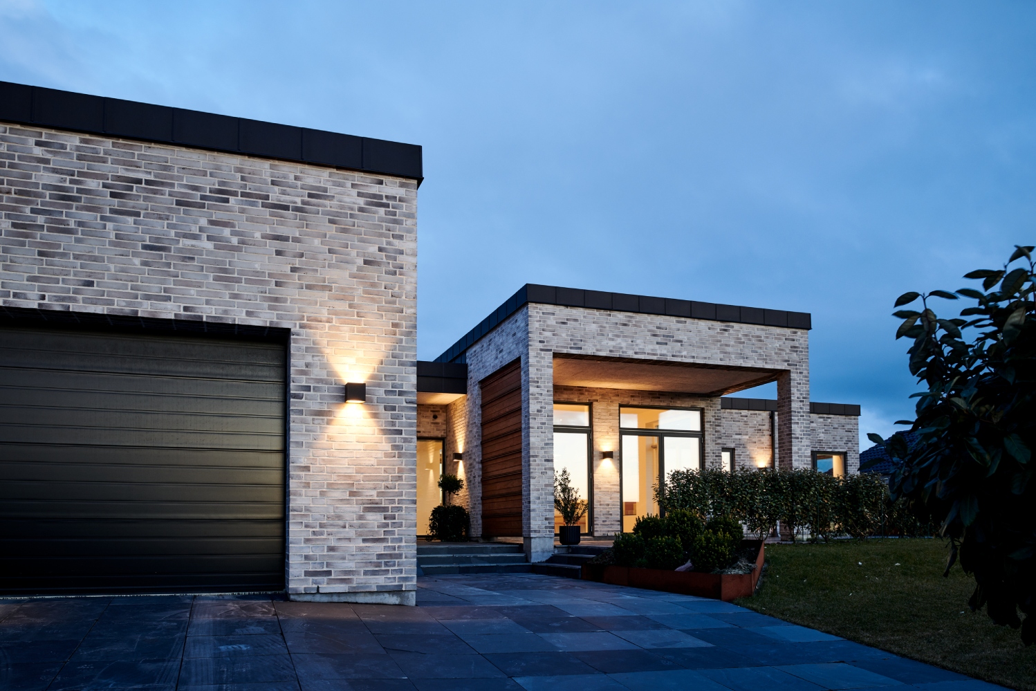 Light-Point Copenhagen CUBE Up Down LED XL wall light in black, casting symmetrical light patterns on a contemporary brick façade at dusk.