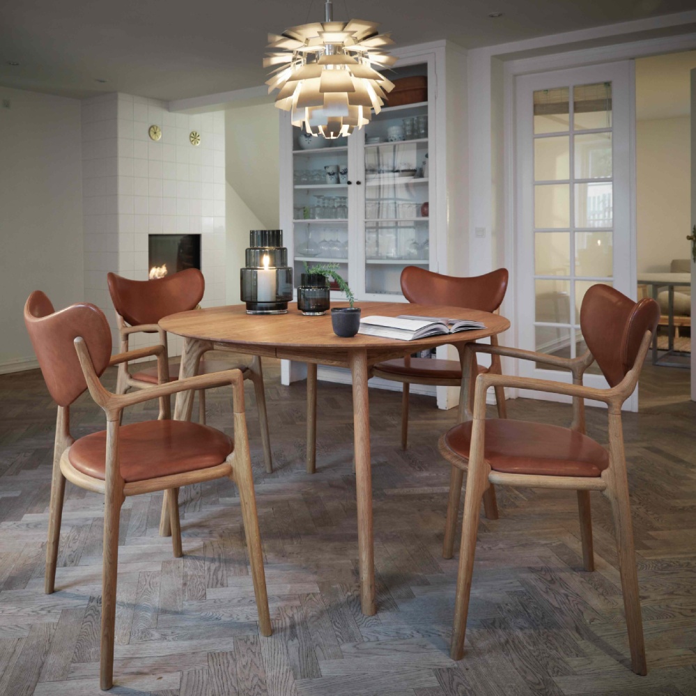 A staged photo in a dining room, Scandinavian style, with salon chairs laid around a salon table. Some Scandinavian design touches, like candles and plants, are scattered throughout.